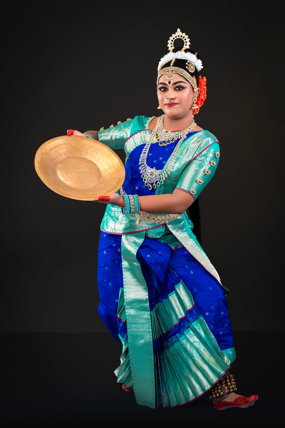 Classical dancer in blue and turquoise holding a brass plate