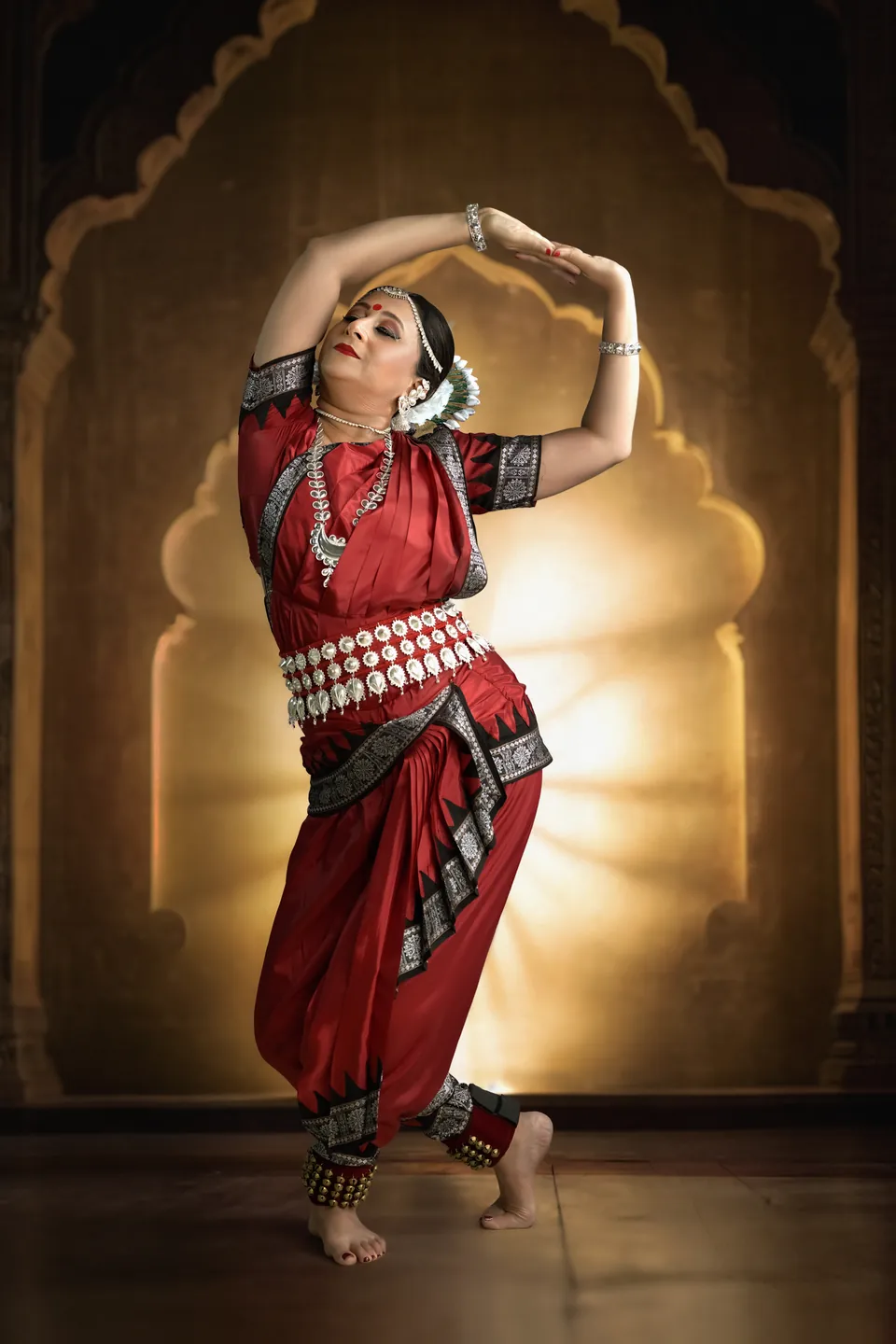 Classical dancer in red posing beneath a glowing ornate arch