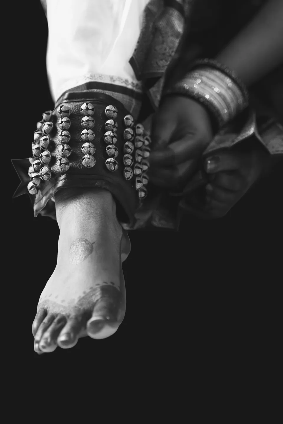 Black-and-white detail of a dancer fastening ankle bells