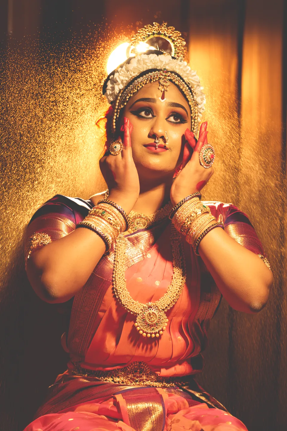 Classical dancer framing her face with both hands in warm golden light