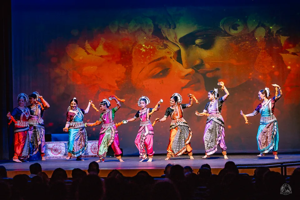 Ensemble of dancers performing across a stage before a colorful backdrop