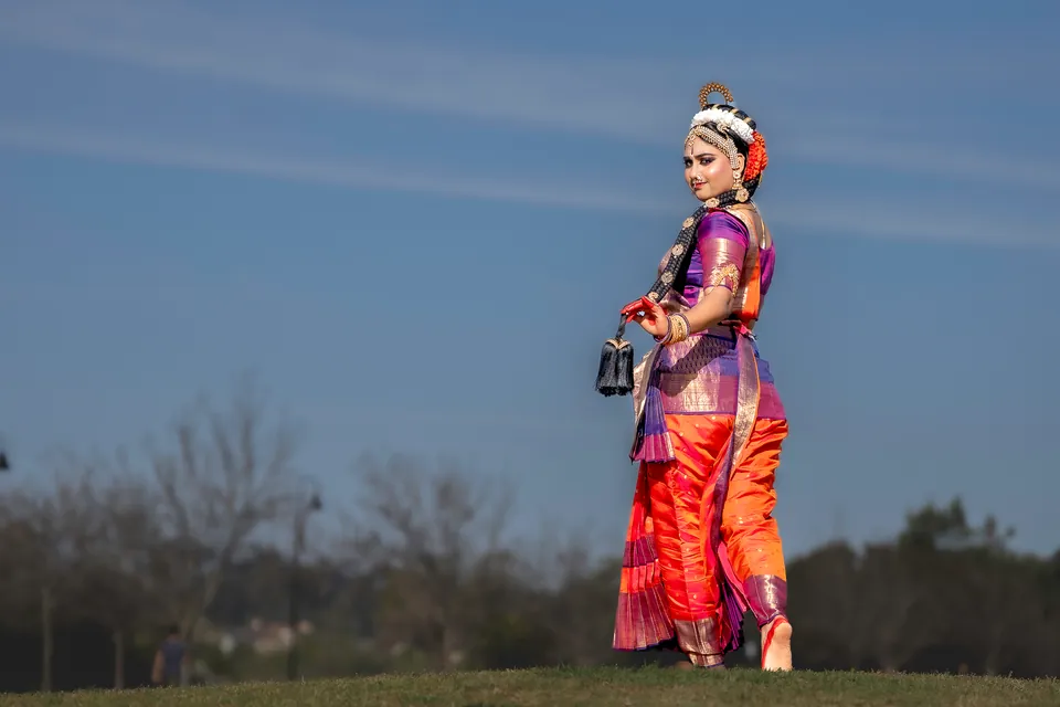 Classical dancer in orange and purple standing outdoors beneath a blue evening sky