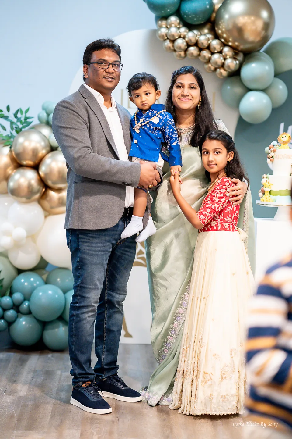 Family posing beside balloons at a first-birthday celebration