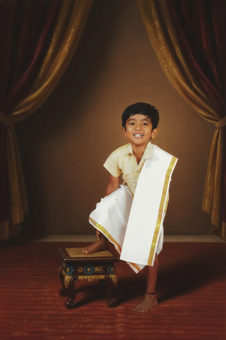 Young boy in traditional clothing seated against warm gold drapery