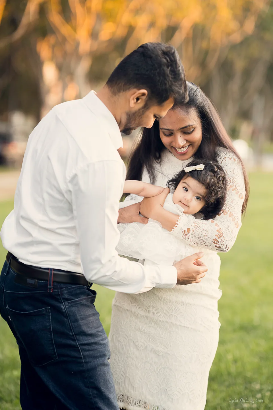 Two parents smiling down at the baby held between them outdoors