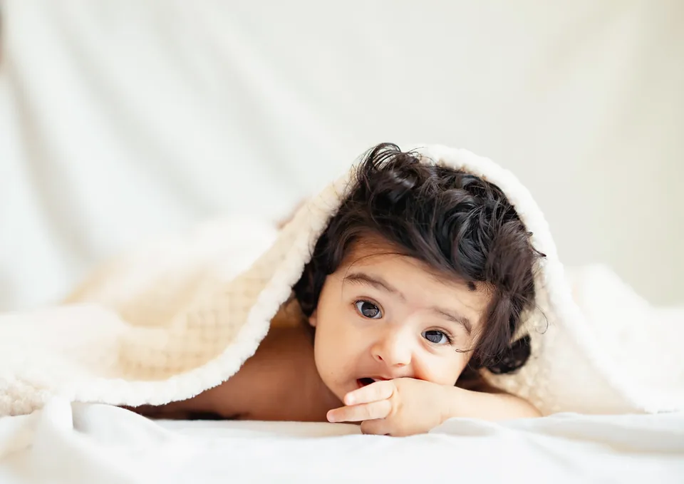 Baby peeking out from beneath a soft cream blanket