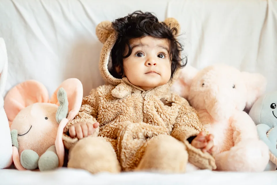 Baby in a soft bear outfit sitting among plush toys