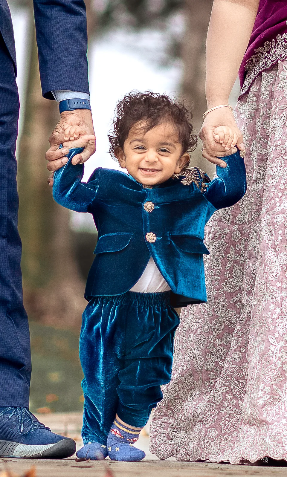 Young child in a blue suit holding two adults by the hands