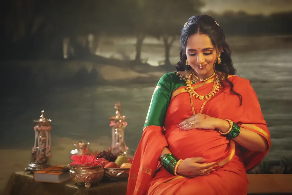 Expectant mother in a red sari smiling down at her belly