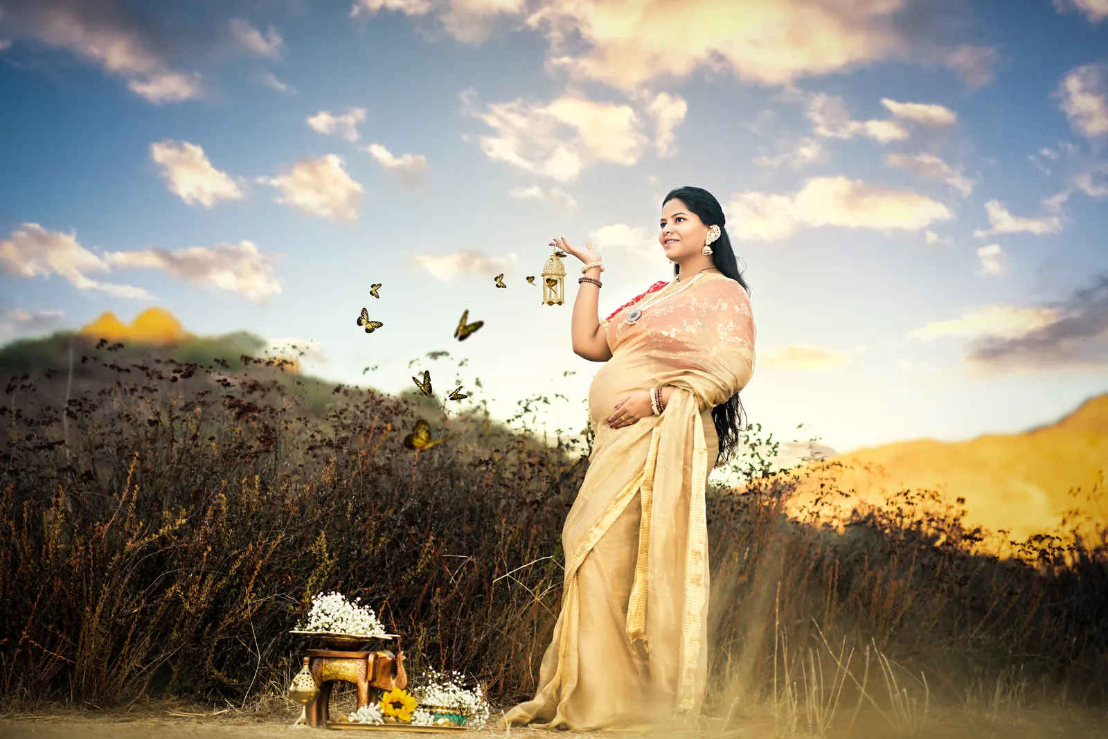 Expectant mother in a gold sari holding a lotus beneath an open sky