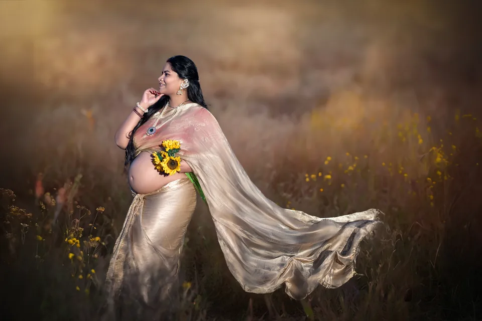 Expectant mother holding a sunflower as a gold drape flows around her