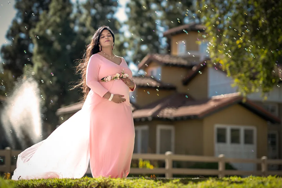 Expectant mother in a pink gown beneath a flowering tree