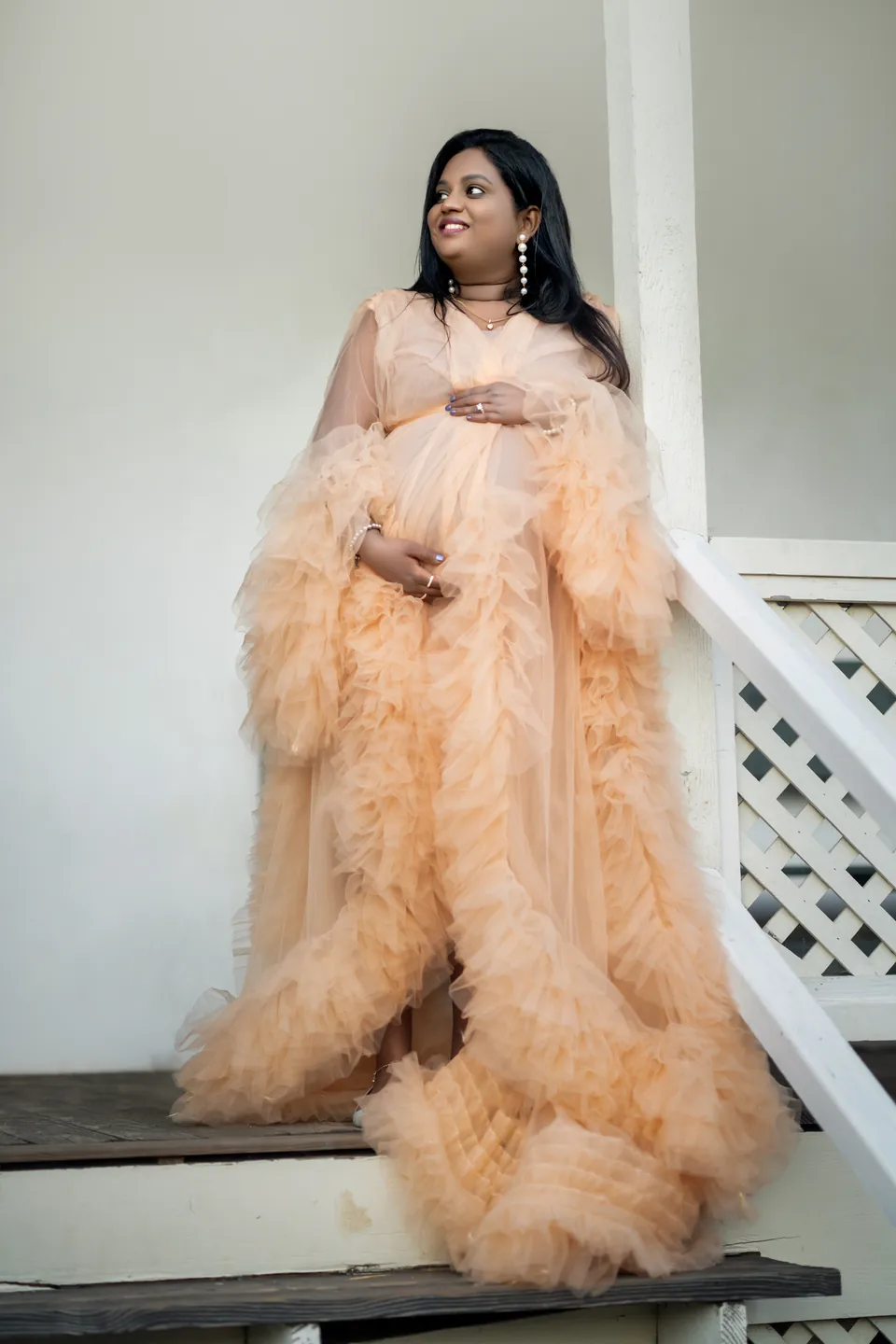 Expectant mother in a textured peach gown beside a white porch