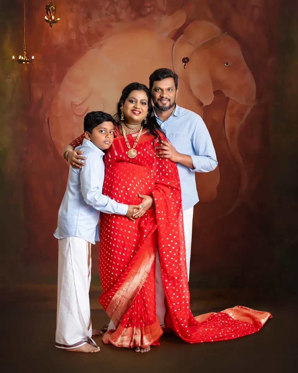 Expectant mother in red standing with her partner and a child against a warm backdrop
