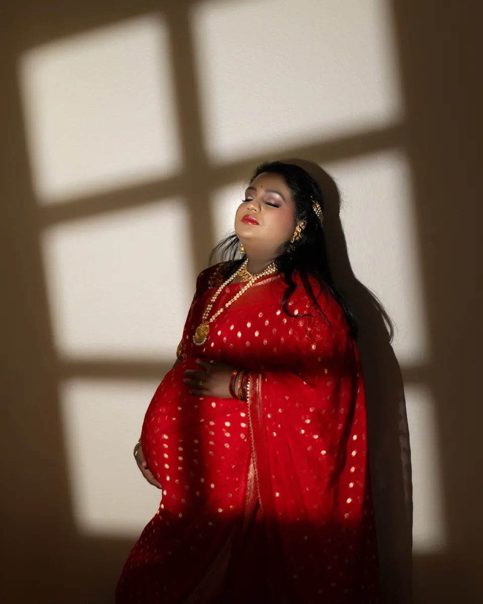 Expectant mother in a red outfit standing in patterned window light