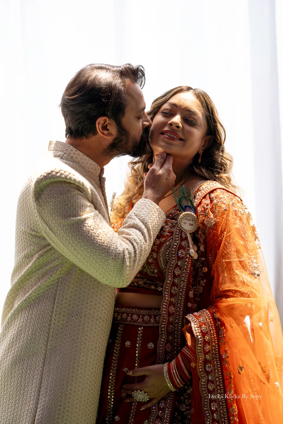 Partner kissing the cheek of a smiling woman in orange and gold wedding attire