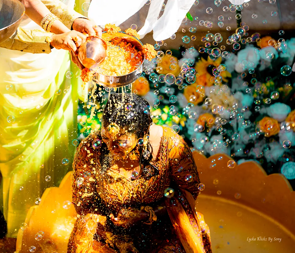Turmeric and water being poured over a person during a pre-wedding celebration