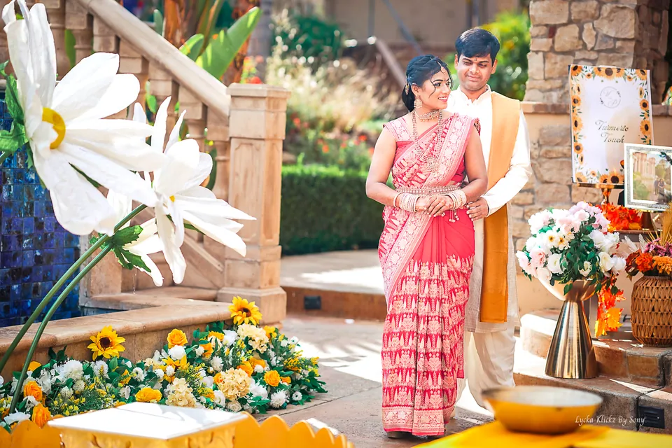 Couple in pink and gold traditional attire surrounded by white floral decorations