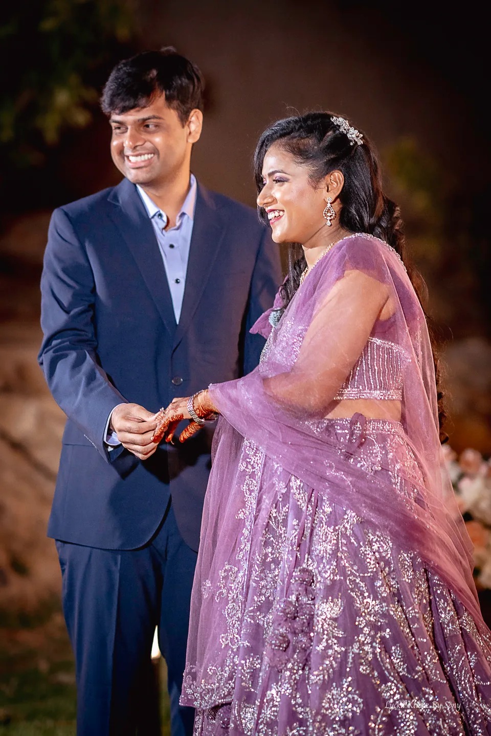 Couple in purple evening attire smiling during their ring ceremony