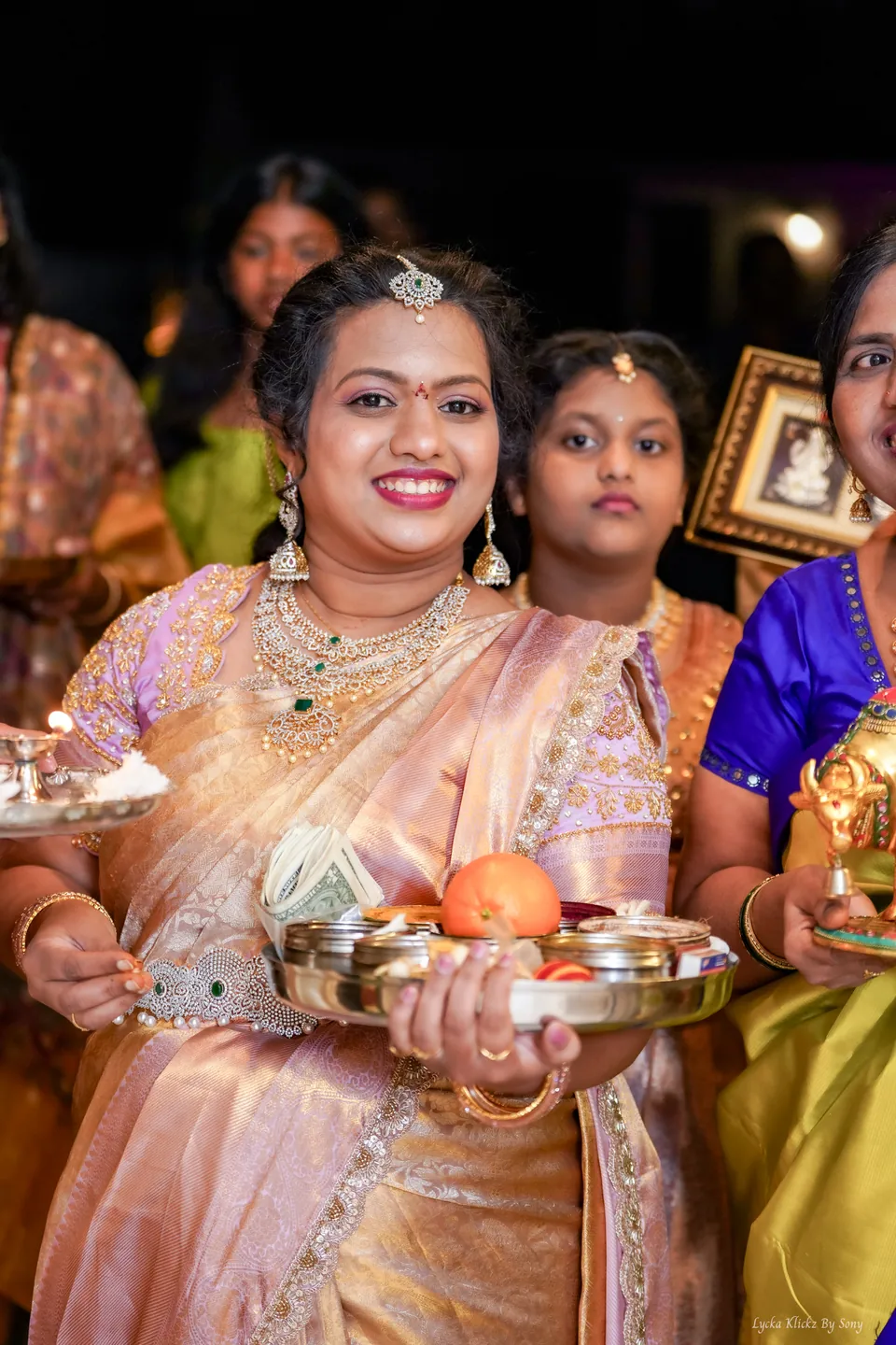 Woman in a pink and gold sari holding a ceremonial tray